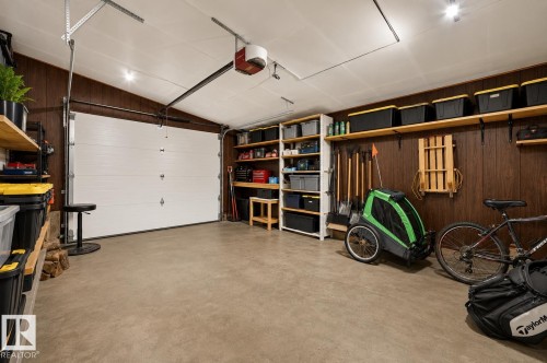 Spacious garage featuring a concrete floor, overhead lighting, wood-paneled walls, and built-in shelving systems - 24 Addison Crescent, St. Albert, AB 