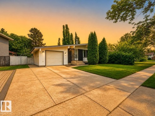 Sleek ranch-style residence featuring a prominent garage door, expansive concrete driveway, and a verdant lawn - 24 Addison Crescent, St. Albert, AB 