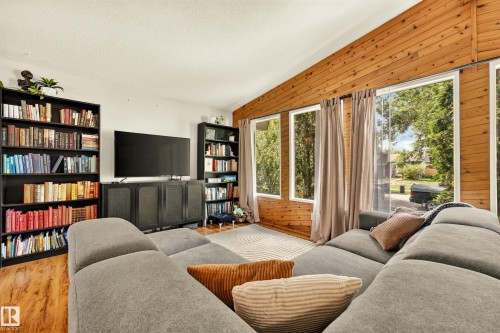 Living area featuring extensive wood-finish wall paneling, multiple large windows, wood-finish flooring, and a white ceiling - 24 Addison Crescent, St. Albert, AB 