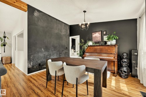 Open-concept dining area featuring wood-finish flooring, a dark accent wall with a chalkboard surface, and a black chandelier - 24 Addison Crescent, St. Albert, AB 