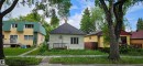 Single-story home featuring light-colored siding, a dark shingled roof, a front porch with a dark railing, and a visible chimney - 12741 117 Street Nw, Edmonton, AB 