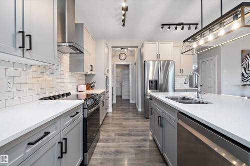 Modern kitchen featuring an expansive center island with an integrated double sink, stainless steel appliances, light gray cabinetry with black hardware, white subway tile backsplash, and wood-finish flooring - 363 Cy Becker Boulevard, Edmonton, AB - Indoor Photo Showing Kitchen With Double Sink With Upgraded Kitchen