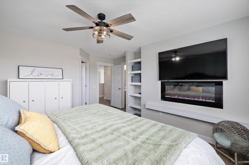 Spacious room featuring an electric fireplace beneath a wall-mounted television, a ceiling fan with integrated lighting, and built-in shelving - 363 Cy Becker Boulevard, Edmonton, AB - Indoor Photo Showing Bedroom