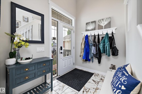 Foyer entrance featuring a glass-paneled entry door with transom window, white marble-style floor tiles, a built-in coat rack shelf, and staircase with white risers - 363 Cy Becker Boulevard, Edmonton, AB - Indoor