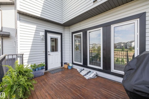 Spacious outdoor deck with rich wood-finish flooring, featuring multiple windows with black trim and white frames, a white entry door, and light-colored siding - 363 Cy Becker Boulevard, Edmonton, AB - Outdoor With Deck Patio Veranda With Exterior