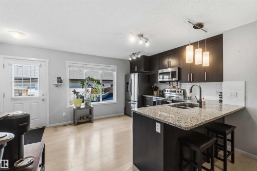 Open-concept kitchen featuring wood-finish flooring and a kitchen island with granite-style countertop - 940 East Gate, Edmonton, AB 