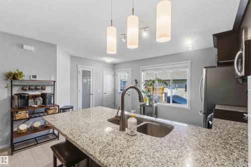 Kitchen island featuring a double basin sink with a gooseneck faucet, light-toned speckled countertop, and recessed bar seating - 940 East Gate, Edmonton, AB 