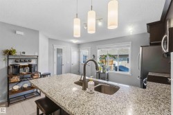 Kitchen island featuring a double basin sink with a gooseneck faucet, light-toned speckled countertop, and recessed bar seating - 
