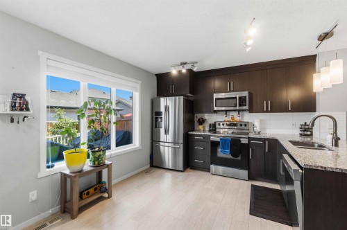 Modern kitchen featuring dark wood-finish cabinetry, stainless steel appliances, granite countertops, and light wood-finish flooring - 940 East Gate, Edmonton, AB 