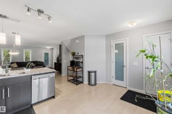 Open-concept living space with light wood-finish flooring, a kitchen island featuring dark cabinetry and light granite-style countertops, stainless steel appliances, and a modern track lighting fixture - 