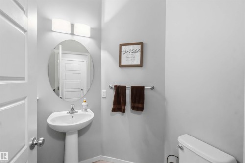 Pedestal sink with an oval mirror, modern wall-mounted light fixture, and light-toned walls - 940 East Gate, Edmonton, AB 