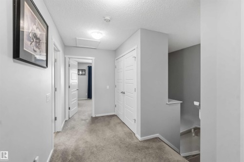Carpeted hallway featuring light gray walls, multiple white panel doors, a ceiling-mounted flush light fixture, and a stairway with a half-wall railing - 940 East Gate, Edmonton, AB 