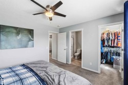 Carpeted room with a ceiling fan featuring integrated lighting, a solid panel door, and an open doorway leading to a closet with built-in shelving - 