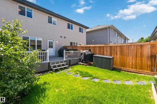Backyard featuring a composite deck with white railings, a well-maintained lawn, stepping stones, and a privacy fence - 940 East Gate, Edmonton, AB 