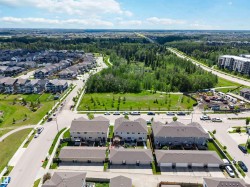 Aerial perspective showcasing a residential community with multiple detached homes and townhomes, surrounded by extensive green spaces and mature trees - 
