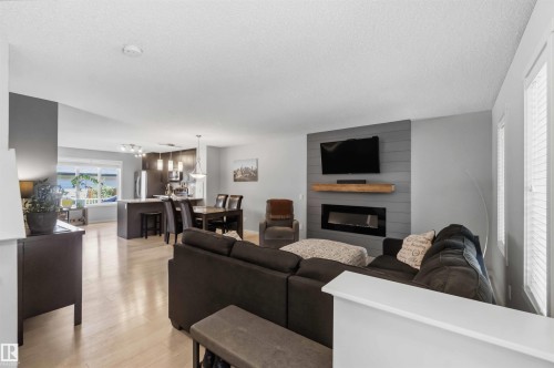 Open-concept living area featuring light wood-finish flooring, a contemporary fireplace with a wood mantle, and a shiplap accent wall - 940 East Gate, Edmonton, AB 