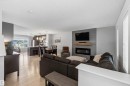 Open-concept living area featuring light wood-finish flooring, a contemporary fireplace with a wood mantle, and a shiplap accent wall - 940 East Gate, Edmonton, AB 