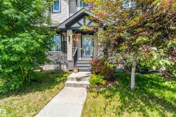 Entryway featuring a grey paneled exterior with stone accents, covered porch with dark railing, glass-paned door, and concrete walkway - 
