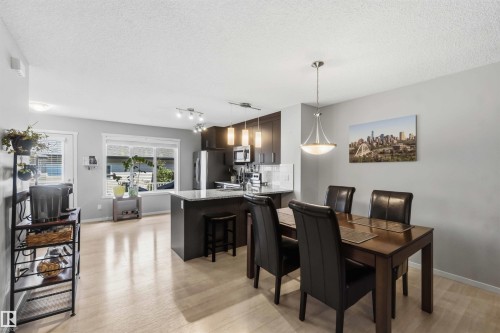 Open-concept living area with light wood-finish flooring, featuring a kitchen island with granite countertop and a dining space with a contemporary pendant light fixture - 940 East Gate, Edmonton, AB 