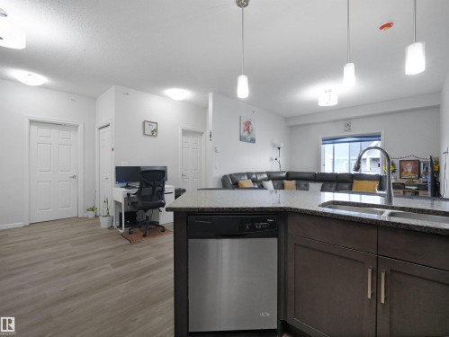 Kitchen island featuring a double basin sink with a high-arc faucet, a stainless steel dishwasher, and dark wood cabinetry - 415 2203 44 Ave, Edmonton, AB 