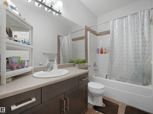 Bathroom featuring a dark wood-finish vanity with an integrated sink, a light-toned countertop, a full-width mirror, and a bathtub with tiled surround - 415 2203 44 Ave, Edmonton, AB 