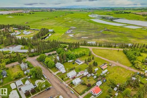 Aerial perspective showcasing a residential area bordered by expansive green fields, mature trees, and several bodies of water - 5305 51 Street, Willingdon, AB 