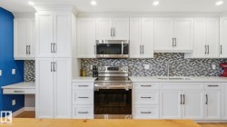 Contemporary kitchen featuring white shaker cabinetry, stainless steel appliances, mosaic tile backsplash, a built-in desk area, and recessed lighting - 