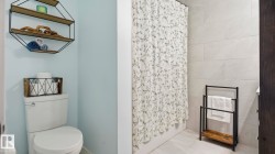 Bathroom featuring light blue wall paint, a white toilet, and gray tiled shower walls - 