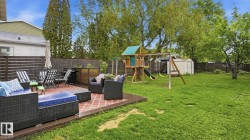 Expansive backyard featuring a brick paver patio, a green lawn, mature trees, a wooden fence, and a storage shed - 