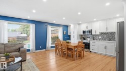 Open-concept living space featuring wood-finish flooring, recessed lighting, and a white kitchen with stainless steel appliances - 
