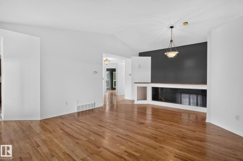 Living area featuring wood-finish flooring, a vaulted ceiling, and a built-in linear fireplace with a dark accent wall - 86 Heritage Crescent, Stony Plain, AB 