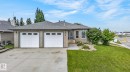 Light brick exterior featuring a two-car garage with panel doors and upper window inserts, a concrete driveway, and a shingled roof - 86 Heritage Crescent, Stony Plain, AB 