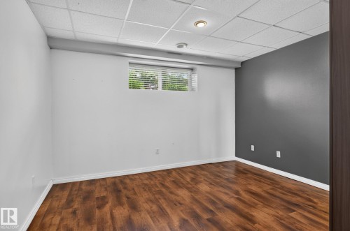 Neutral-toned room featuring wood-finish flooring, a drop ceiling with recessed lighting, and a window with blinds - 86 Heritage Crescent, Stony Plain, AB 