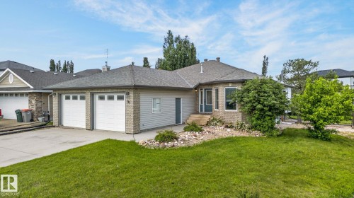 Ranch-style residence featuring a two-car garage with panel doors, light brick facade, and a shingled roof - 86 Heritage Crescent, Stony Plain, AB 