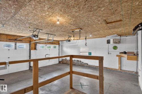 Spacious garage with exposed OSB ceiling, two overhead doors with automatic openers, concrete flooring, and a built-in workbench - 86 Heritage Crescent, Stony Plain, AB 