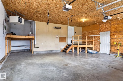 Spacious garage featuring a concrete floor, exposed wood ceiling, built-in workbench, elevated platform with stairs, and two overhead garage door openers - 86 Heritage Crescent, Stony Plain, AB 