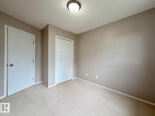 Neutral-toned room featuring a ceiling-mounted light fixture, light beige carpeting, white baseboards, and two white doors with matching trim - 12207 16 Avenue, Edmonton, AB 