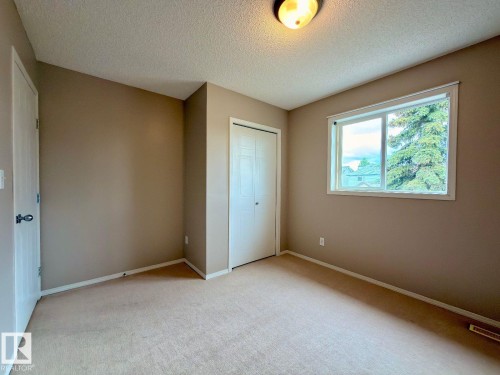 Neutral-toned room featuring a single window, a flush-mount ceiling light fixture, and textured carpeting - 12207 16 Avenue, Edmonton, AB 