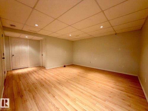 Spacious room featuring light wood-finish flooring, a grid-panel ceiling with recessed lighting, and neutral wall paint - 12207 16 Avenue, Edmonton, AB 