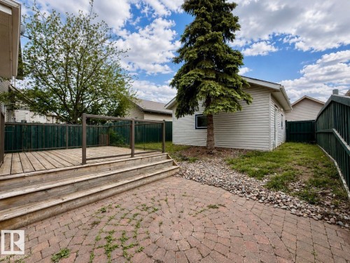 Outdoor living space featuring a wood deck with glass panel railing, a paver patio, and a detached building with horizontal siding - 12207 16 Avenue, Edmonton, AB 