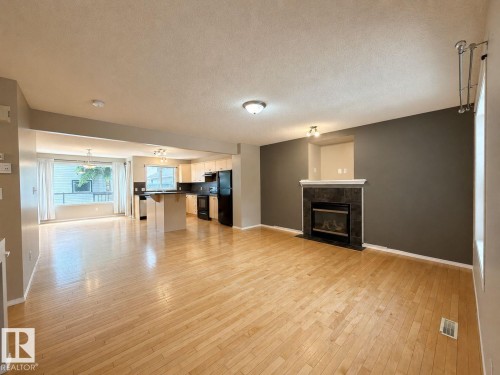 Open-concept living space featuring wood-finish flooring, a stone-clad fireplace with a white mantel, and recessed lighting - 12207 16 Avenue, Edmonton, AB 
