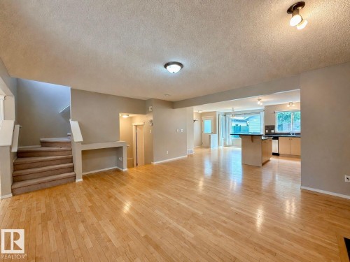 Spacious living area featuring wood-finish flooring, neutral wall tones, and a carpeted staircase - 12207 16 Avenue, Edmonton, AB 