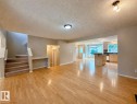 Spacious living area featuring wood-finish flooring, neutral wall tones, and a carpeted staircase - 12207 16 Avenue, Edmonton, AB 