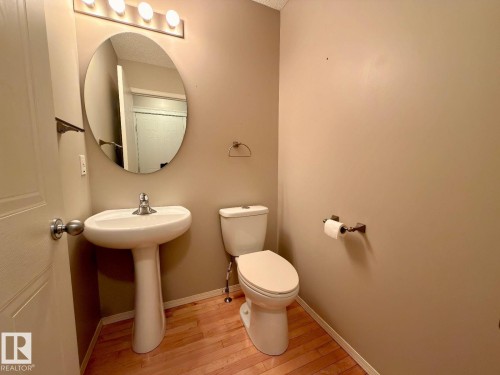 Powder room featuring a white pedestal sink with a chrome faucet, oval frameless mirror, and a four-light vanity fixture - 12207 16 Avenue, Edmonton, AB 