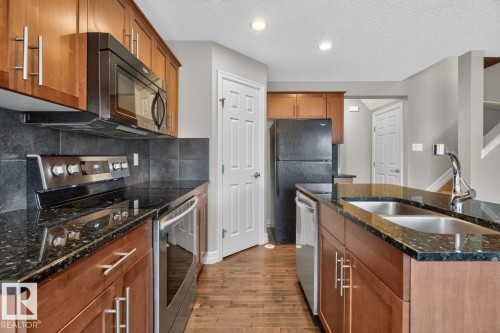 Kitchen featuring wood-finish cabinetry, dark granite countertops, stainless steel appliances, and a double basin sink - 12032 167B Avenue, Edmonton, AB 