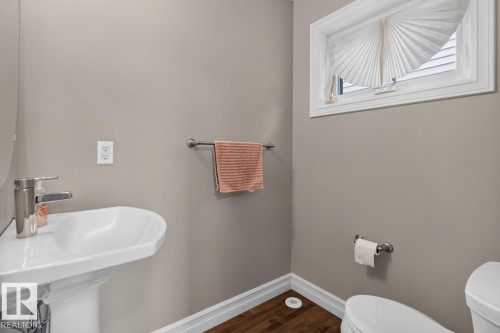 Pedestal sink with a brushed nickel faucet, wood-finish flooring, and a window with pleated blinds - 12032 167B Avenue, Edmonton, AB 