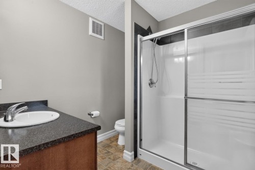 Full bathroom featuring a shower stall with frosted glass doors, a vanity with a dark countertop, an undermount sink, and durable tile flooring - 12032 167B Avenue, Edmonton, AB 