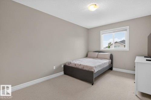 Light-filled bedroom featuring a window with white trim, neutral-toned carpeting, off-white walls, and a ceiling-mounted light fixture - 12032 167B Avenue, Edmonton, AB 