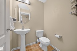 Powder room featuring a pedestal sink with a chrome faucet, oval mirror, and wood-finish flooring - 