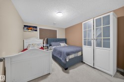 Carpeted bedroom featuring neutral-toned walls, a textured ceiling, and a built-in wardrobe with glass-paneled doors - 